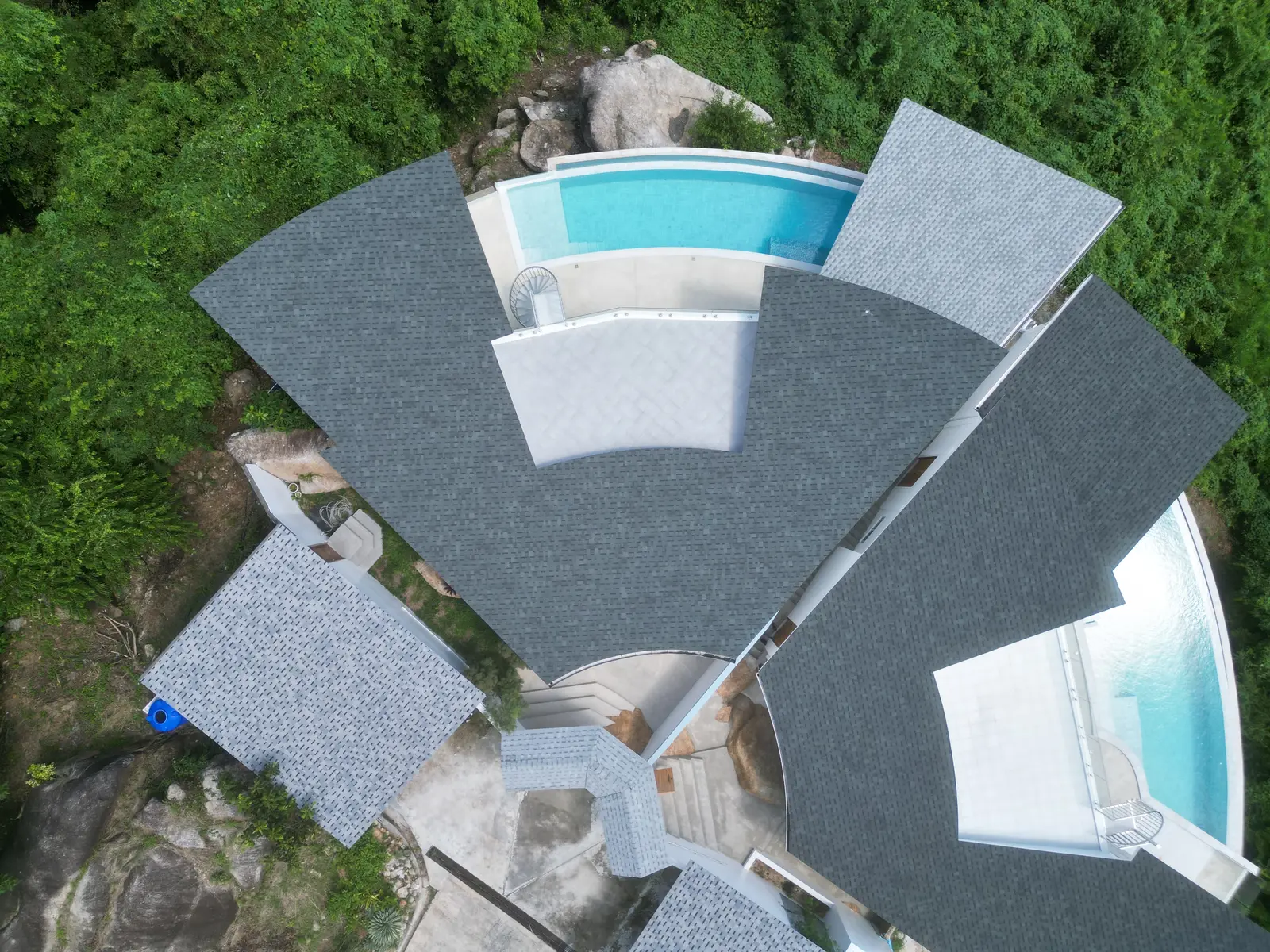 Villa Emerald from directly above — fan of grey roofs and two pools between granite and green